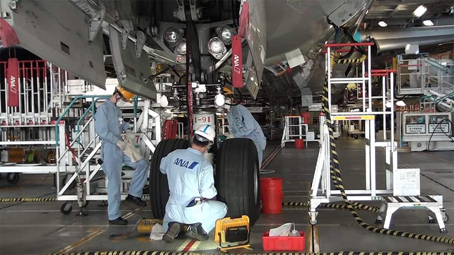飛行機の前脚付近で作業する整備士たちの写真