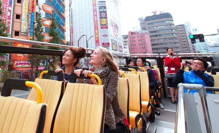 (photo) Passengers are sitting in seats on the top deck of the bus and looking at cityscape.