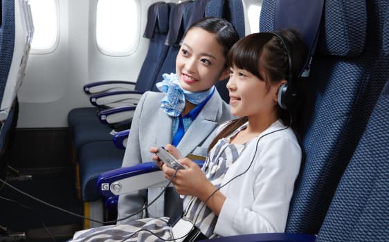 機内エンターテインメントを視聴する少女と客室乗務員